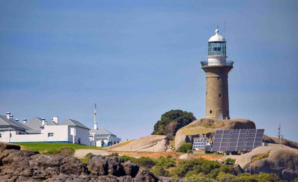 A lighthouse on a rocky island with a white building nearby.