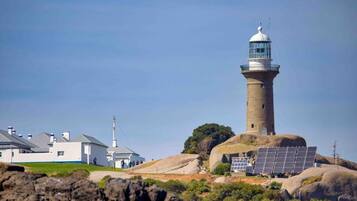 A lighthouse on a rocky island with a white building nearby.