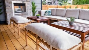 Un patio con chimenea de piedra, mobiliario de madera y vistas a una casa y árboles.