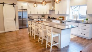Una cocina moderna con armarios blancos, una isla central con taburetes de bar, electrodomésticos de acero inoxidable e iluminación colgante.