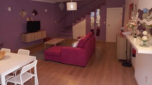 A compact living space with a staircase, a sofa, a TV, and a dining area.
