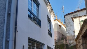 A narrow cobblestone alley with white buildings, including a building with barred windows and a visible electrical box.