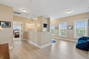 A spacious living area with hardwood flooring, a blue bean bag, and a kitchen area with a flat-screen TV. - Oceanfront, Large Screen Porch, Gas Grill, Luxury Family Rental (Folly Beach)