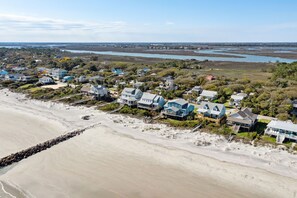 A coastal residential area with houses near the beach, featuring a mix of single and multi-story buildings, some with visible decks and porches.