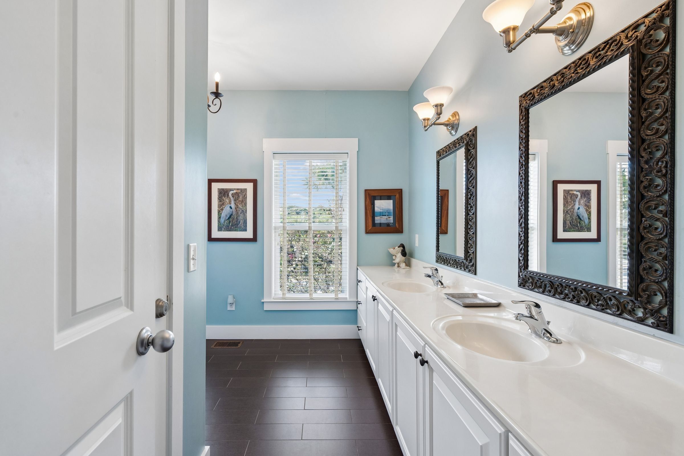 Une salle de bain avec deux lavabos, un grand miroir et une fenêtre avec des stores.