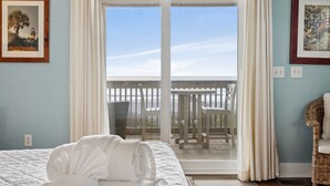 Un dormitorio con cama, vista al balcón y dos cuadros en las paredes.