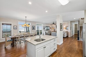 A spacious kitchen with a large island, wooden flooring, and a view of the ocean through the windows. - Oceanfront, Large Screen Porch, Gas Grill, Luxury Family Rental (Folly Beach)