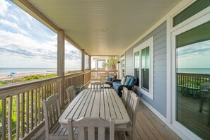 A covered outdoor area with a table and chairs, overlooking a beach.