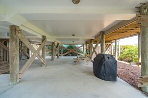 An interior space with a concrete floor, wooden beams supporting a ceiling, and a picnic table. - Oceanfront, Large Screen Porch, Gas Grill, Luxury Family Rental (Folly Beach)