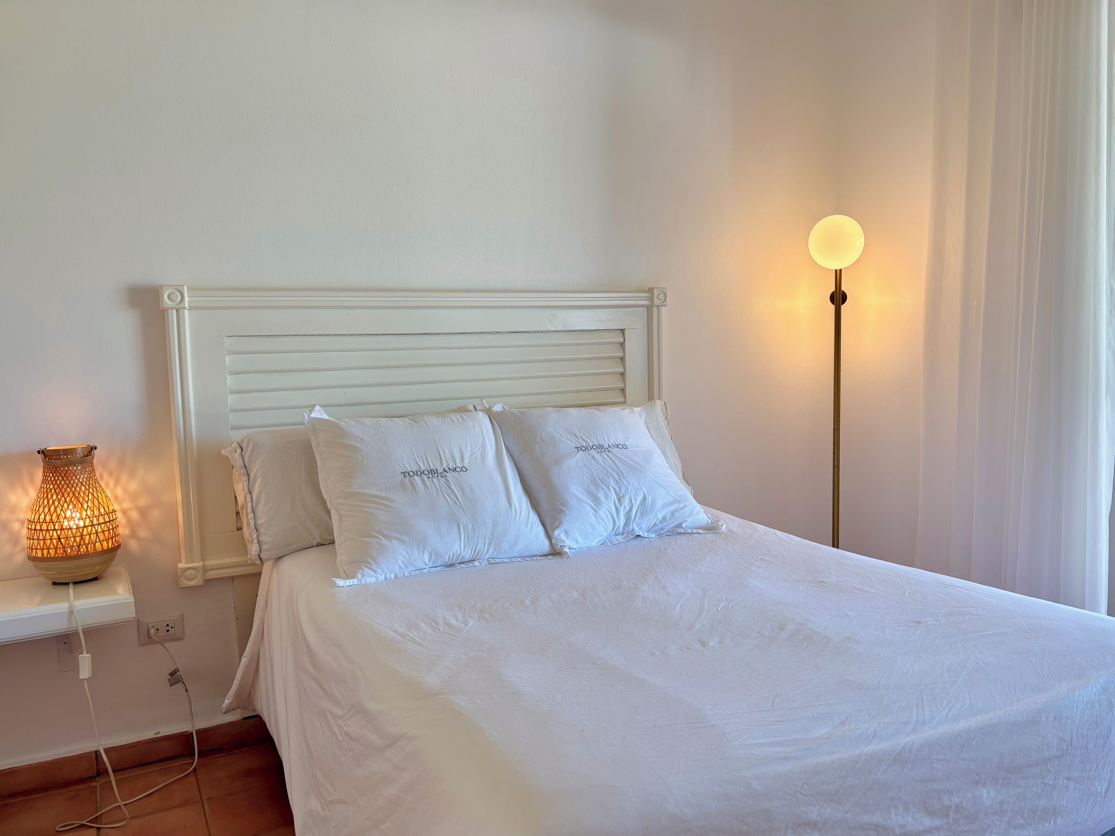 Ein Bett mit weißer Bettwäsche und Kissen, ein Nachttisch mit einer Lampe und eine Steckdose.