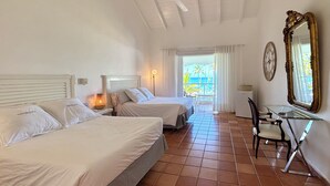 A hotel room with two beds, a desk, a chair, a ceiling fan, a large mirror, and a view of the ocean. - HOTEL TODOBLANCO (Las Galeras)