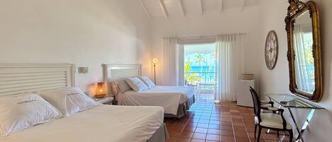 Une chambre d’hôtel avec deux lits, un bureau, une chaise, un ventilateur de plafond, un grand miroir et une vue sur l’océan.