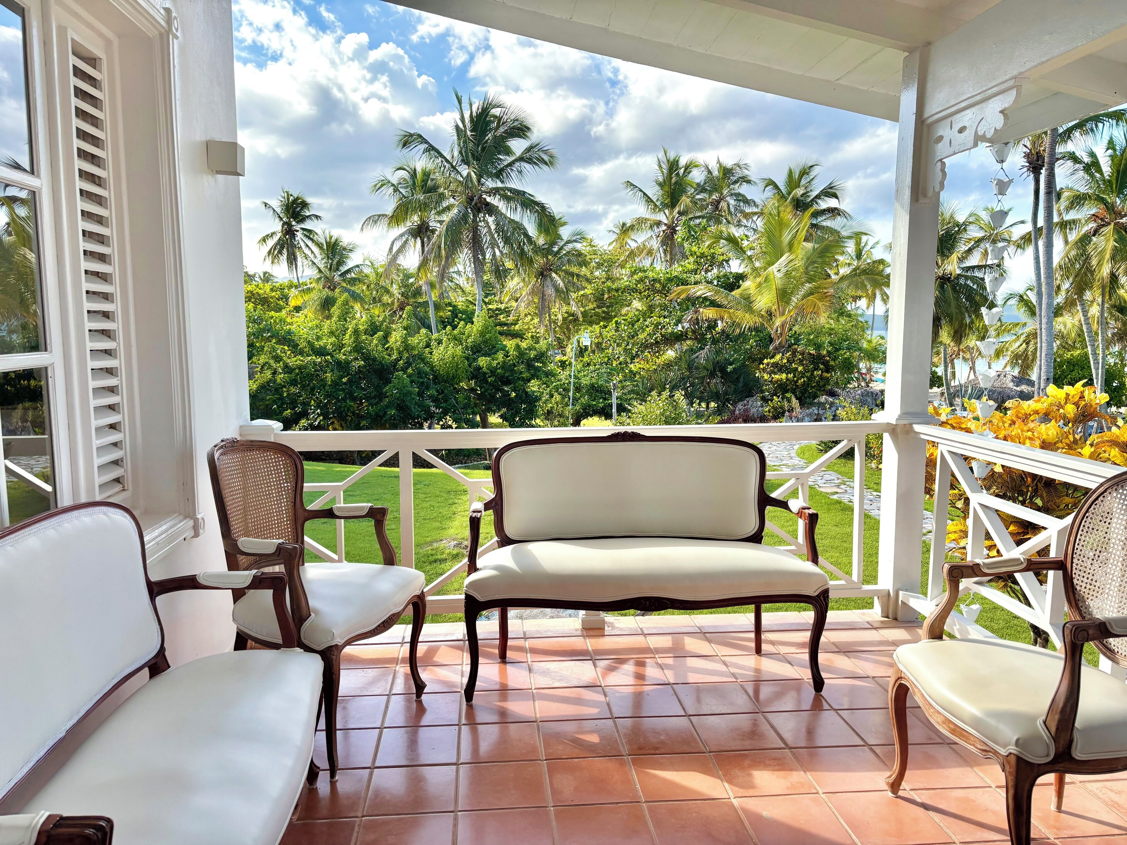 Un espace extérieur abrité, doté de chaises et offrant une vue sur des palmiers et une végétation luxuriante.