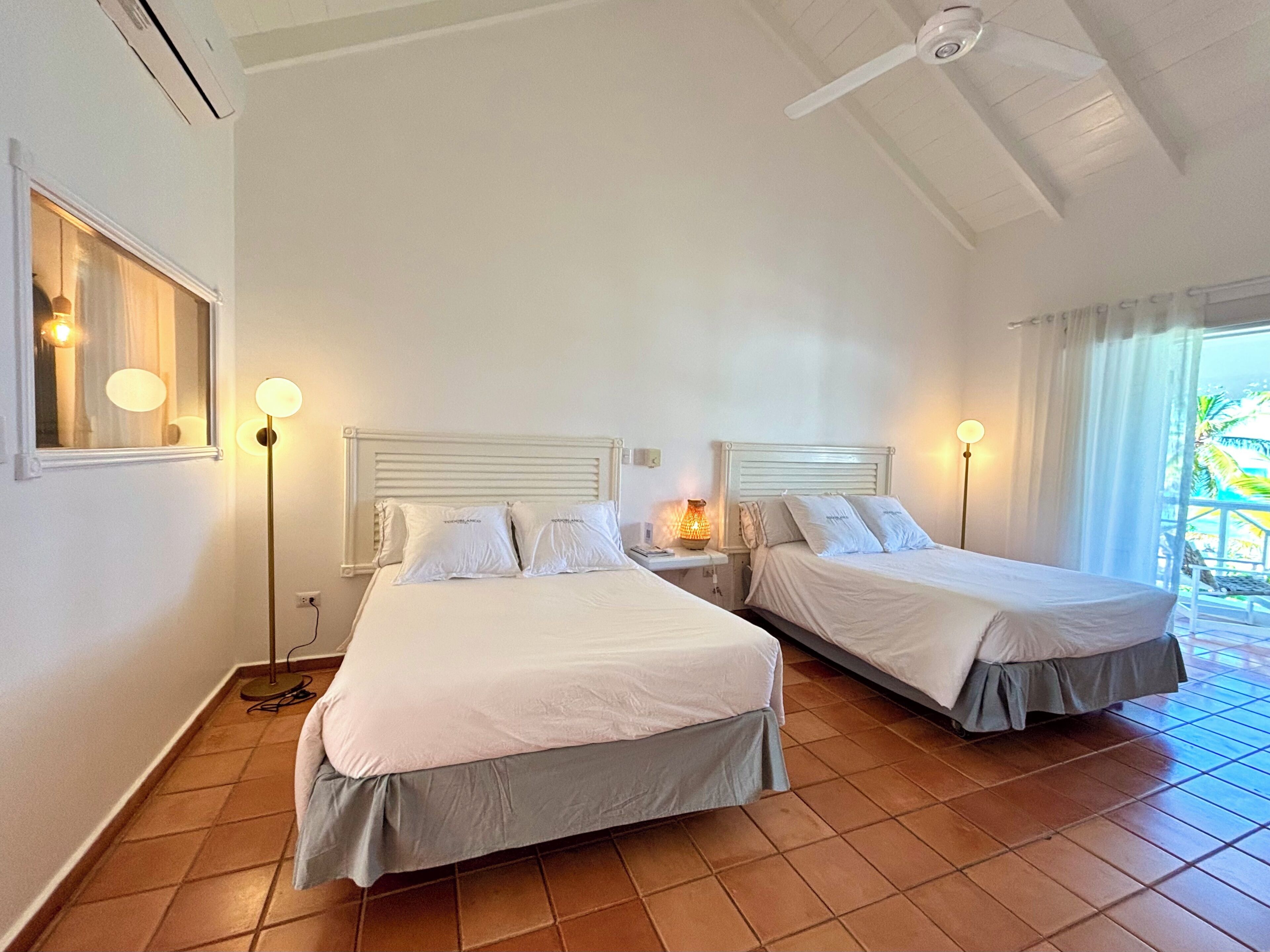 Ett hotellrum med två sängar, en takfläkt och ett fönster med gardiner.