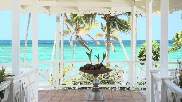 A covered outdoor area with a wooden floor, a central decorative bowl, and a view of the ocean and palm trees. - HOTEL TODOBLANCO (Las Galeras)