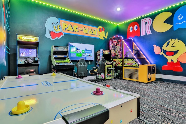 A room with a foosball table, arcade games, and a large screen.