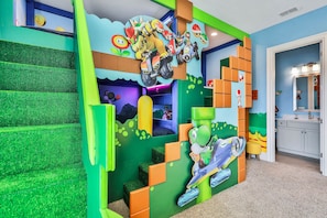 A children's play area with a Mario-themed wall, green steps, and a small table with toys.