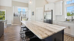 A modern kitchen with a marble island, stainless steel appliances, and a staircase leading to a loft bedroom. - Sound Views, Hot Tub, Village at Ocean Hill, Community Pools (Corolla)