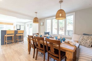 A dining area with wooden chairs and a table, a kitchen with a refrigerator, and a large window with a view.