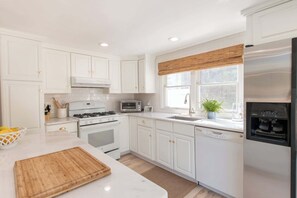 Una cucina moderna con mobili bianchi, un frigorifero in acciaio inossidabile, un forno a microonde e un piano cottura.