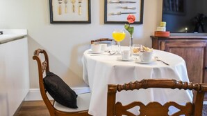 Un comedor con una mesa redonda preparada para dos personas, mantel blanco y un jarrón con una sola flor.