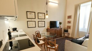 Una sala de estar moderna con una mesa de comedor de vidrio, sillas de madera, un sofá, un televisor y cuadros enmarcados en la pared.