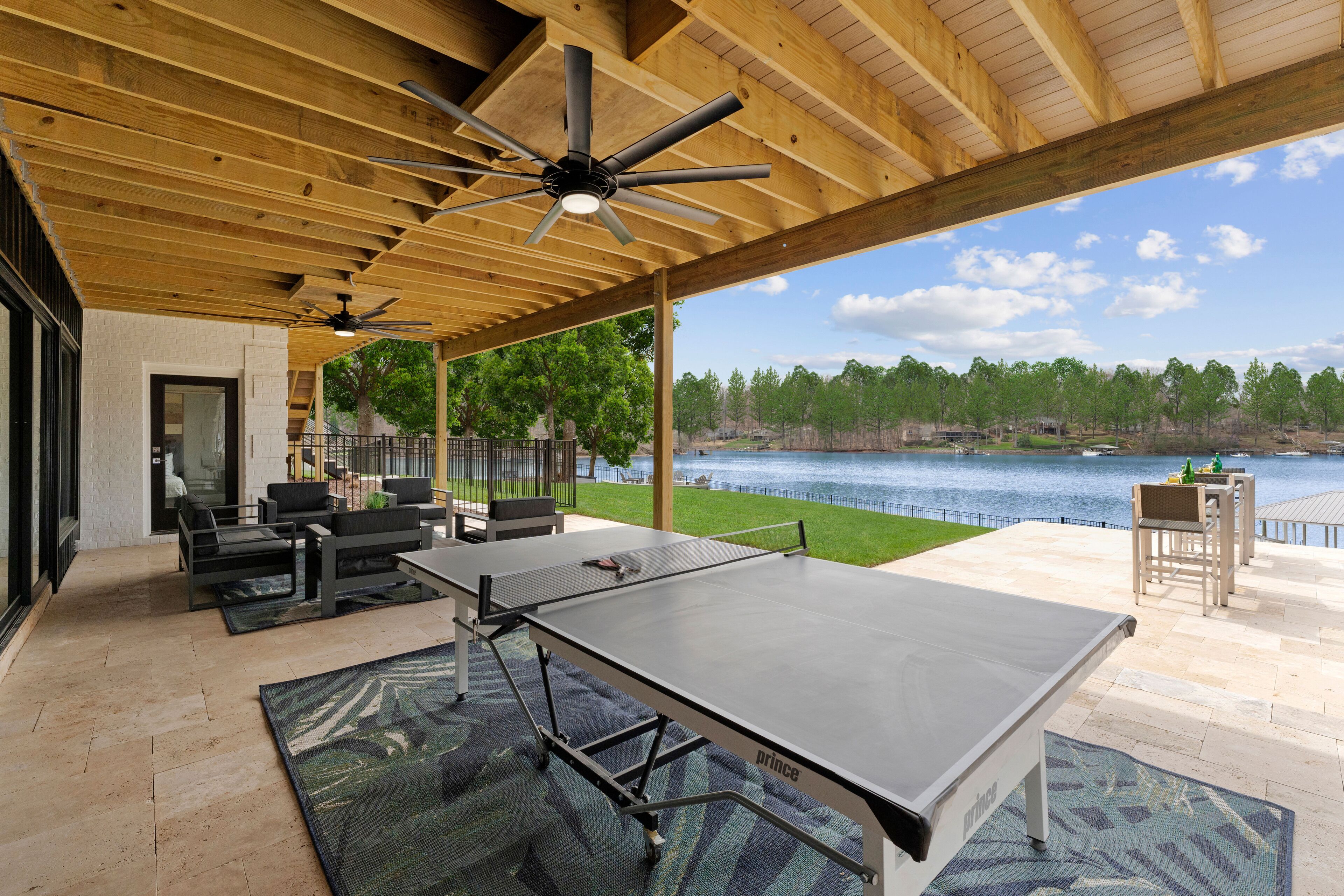 An outdoor patio with a ping pong table, seating, and a view of a lake.