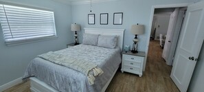 Quarto com uma cama, duas mesas de cabeceira com luminárias, um criado-mudo e uma porta que dá para outro cômodo.
