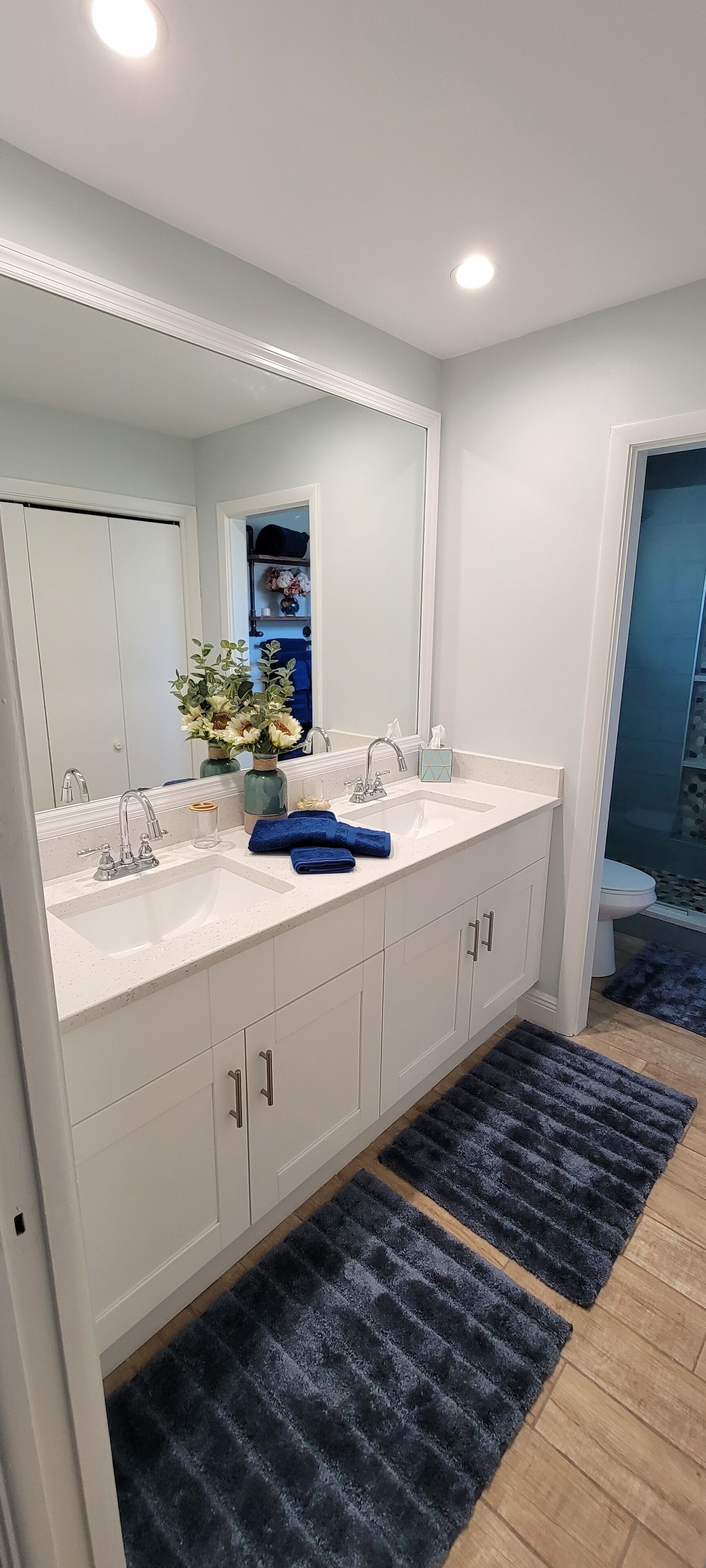 A modern bathroom with a white vanity, a large mirror, and a blue rug on the floor.