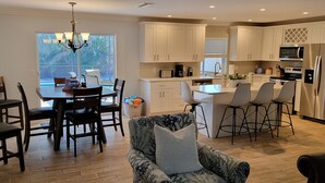 Una cocina moderna con armarios blancos, un refrigerador de acero inoxidable y un comedor con candelabro.
