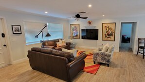 Una sala de estar con un sofá de cuero marrón, un sillón estampado y una zona de comedor con mesa y sillas de madera.