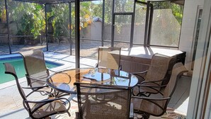 Un patio cubierto con cerramiento de vidrio, una piscina y mobiliario exterior.