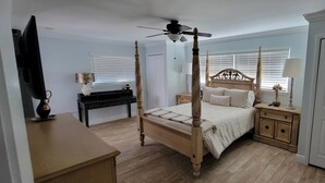Una cama con dosel, un ventilador de techo, una mesita de noche con lámpara, un aparador y un armario.
