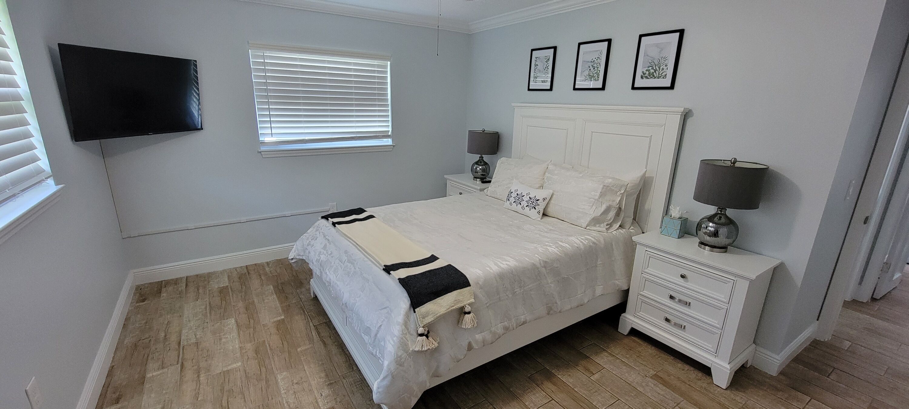 Een slaapkamer met een bed, nachtkastjes, een televisie en een raam met jaloezieën.