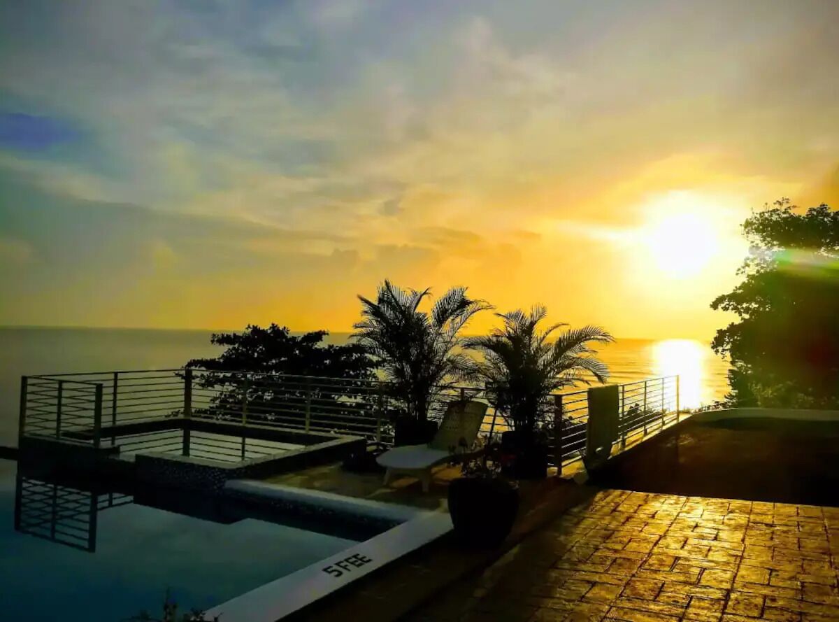 A rooftop pool area with lounge chairs and a view of the sunset over the ocean.