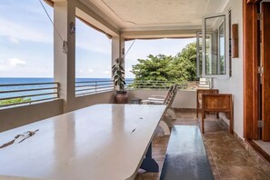 A covered balcony with a table and chairs, a potted plant, and a view of the ocean. - Braata @ Little Bay (Ocean View Villa) (Port Maria)