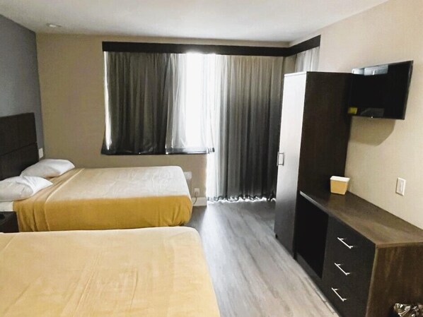 Habitación de hotel con dos camas, un televisor y un ventanal grande con cortinas.