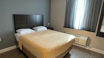 A bedroom with a bed, a headboard, a window with curtains, and a radiator.