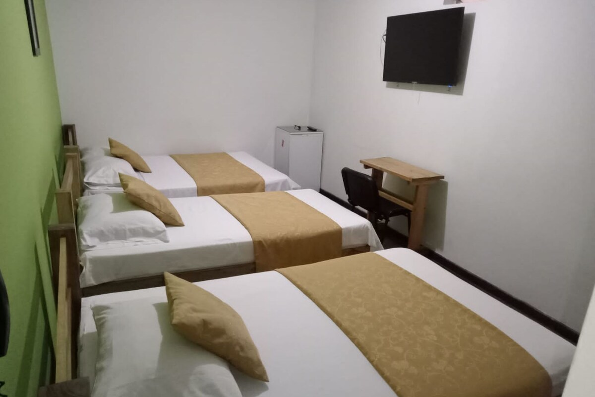 A hotel room with three beds, a desk, and a television.