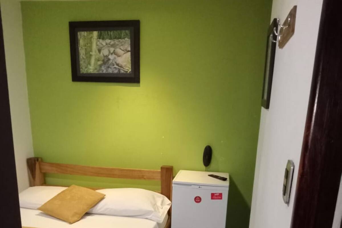 A small, compact room with two beds, a small refrigerator, and a framed picture on the wall.