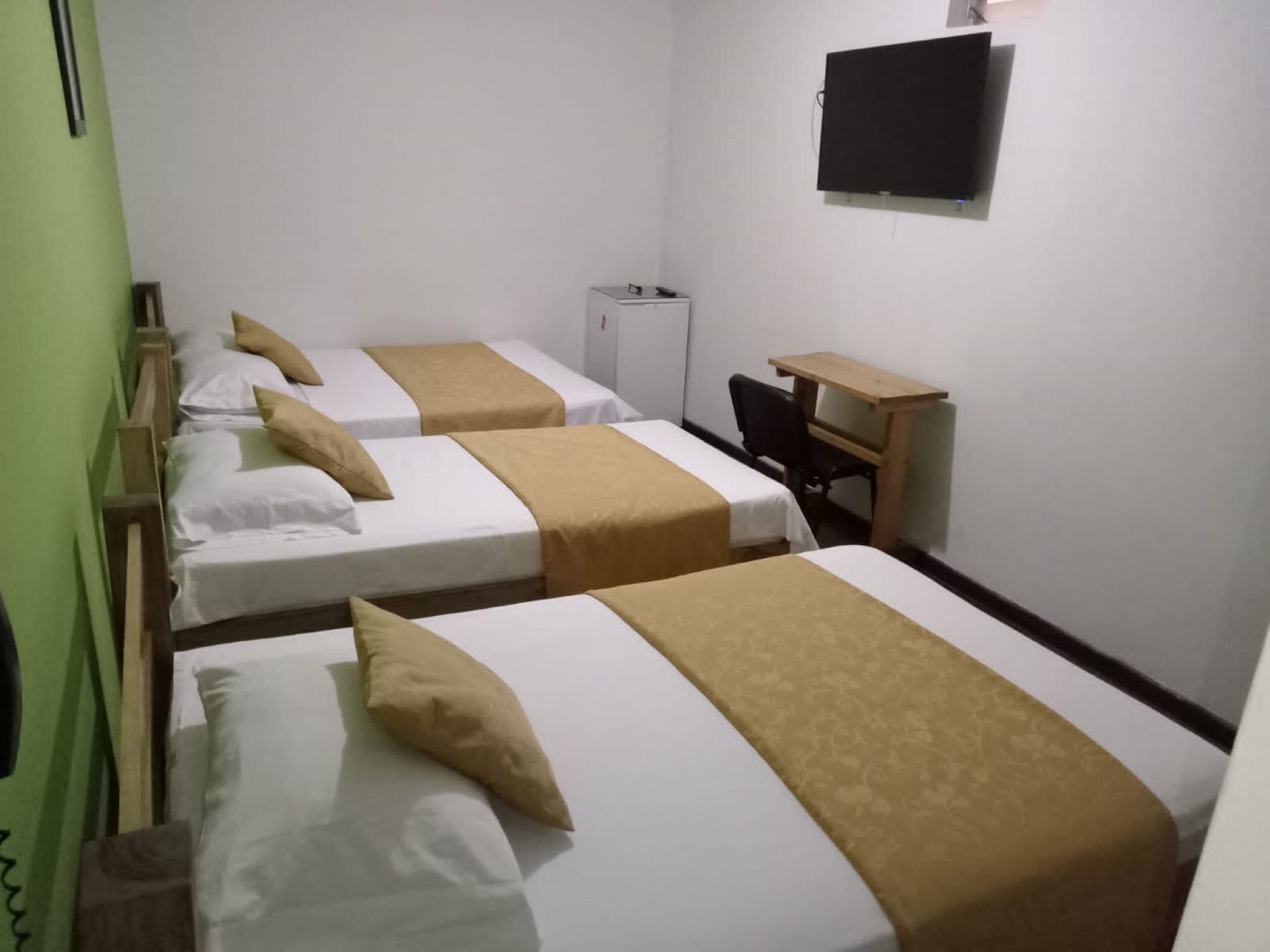 A hotel room with three beds, a desk, and a television.