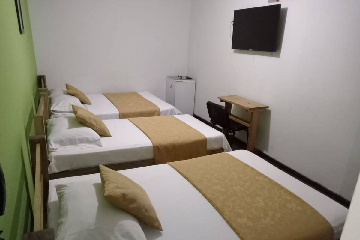 A hotel room with three beds, a desk, and a television.