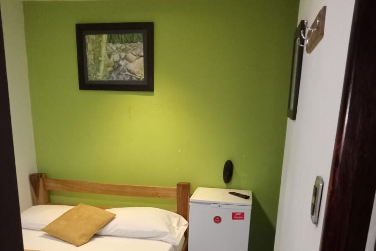 Una habitación pequeña y funcional con dos camas, un refrigerador pequeño y un cuadro en la pared.