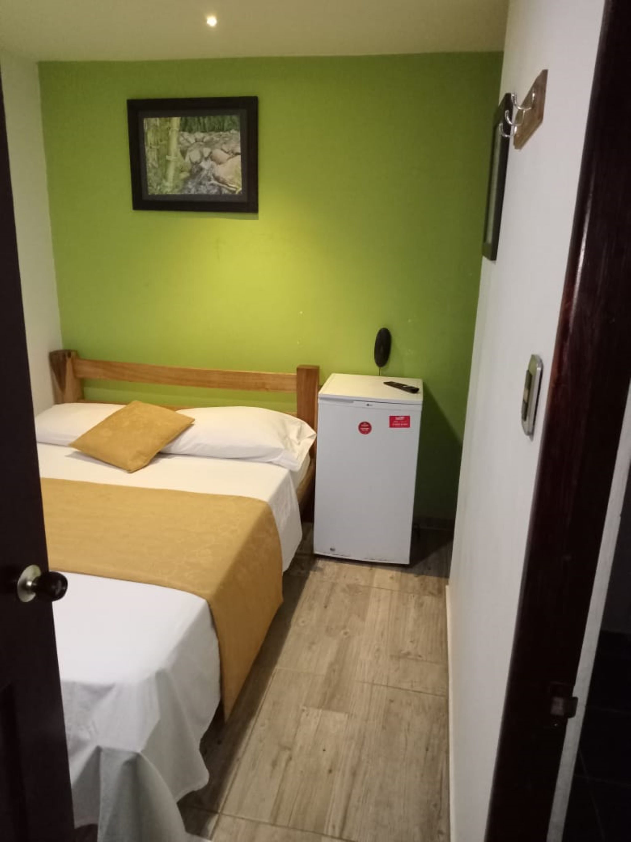 A small, compact room with two beds, a small refrigerator, and a framed picture on the wall.