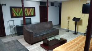 A room with a grey sofa, a small TV, a painting, a floor lamp, and a patterned rug. - Hotel Cañaveral Plaza (Manizales)