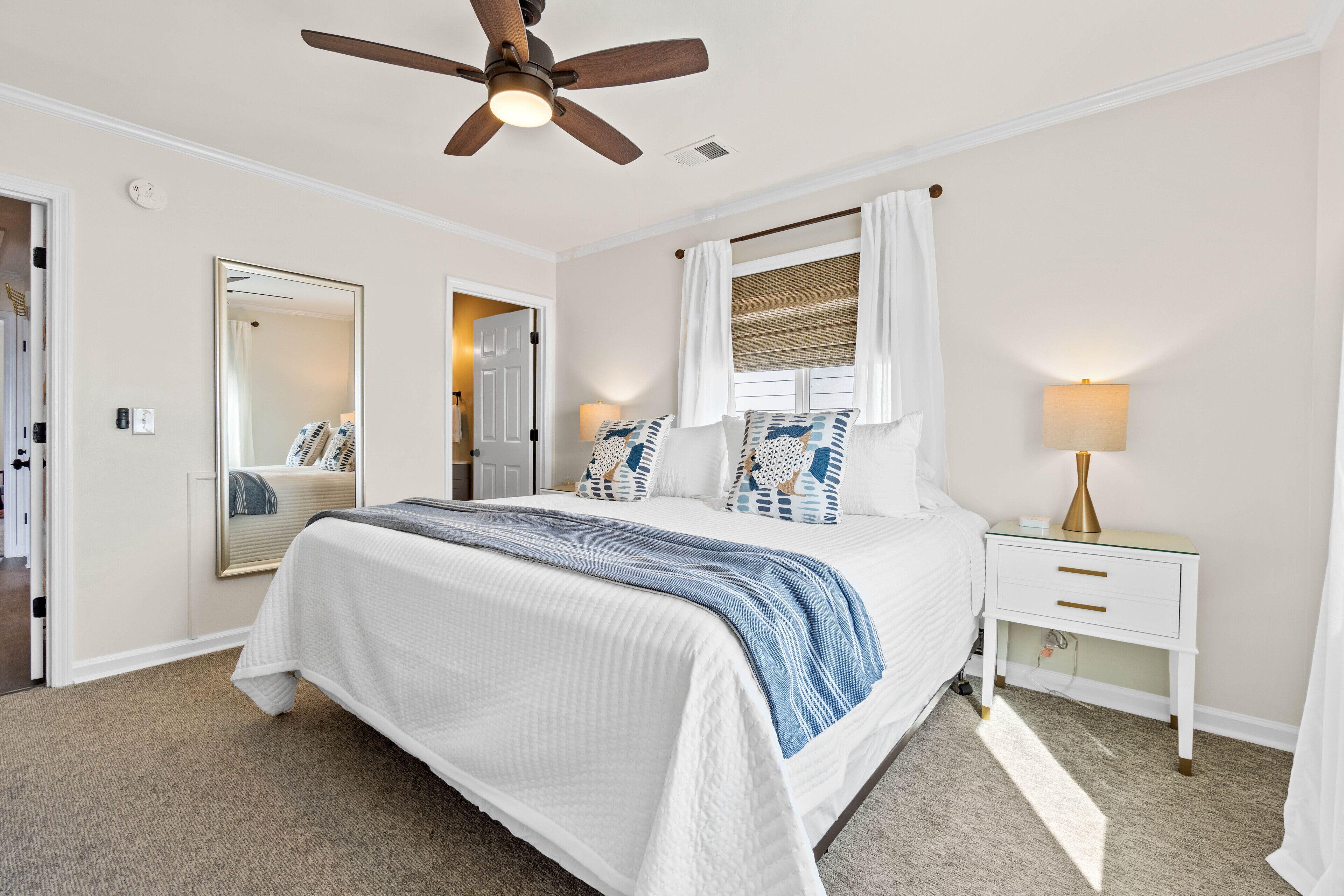 A bedroom with a bed, a nightstand, a ceiling fan, a mirror, and a window with curtains.