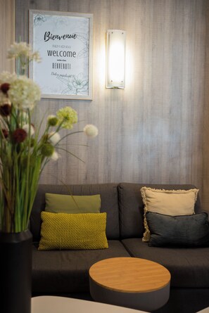 A modern living room with a grey sofa, a round wooden coffee table, and a wall-mounted light fixture.