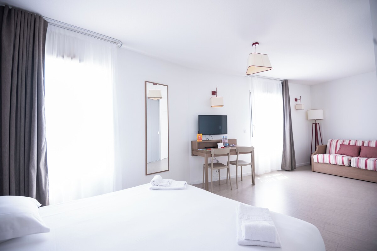 Une chambre d’hôtel avec un grand lit, un bureau avec une télévision et un canapé.