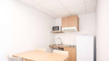 A small kitchen with a microwave, sink, and refrigerator. There is a wooden table with chairs.