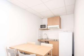 Una cocina pequeña con microondas, fregadero y refrigerador. Hay una mesa de madera con sillas.